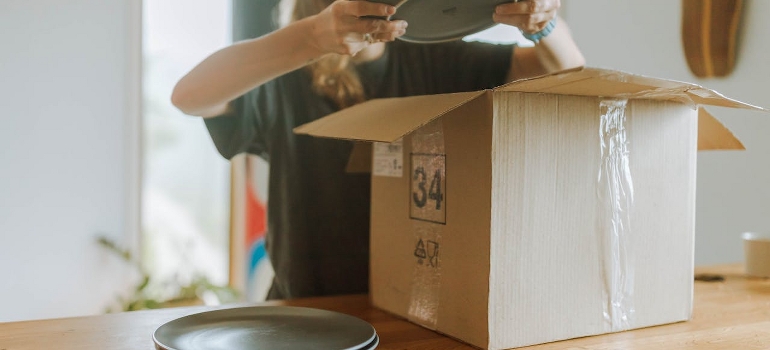 A woman is packing green plates in a cardboard box.