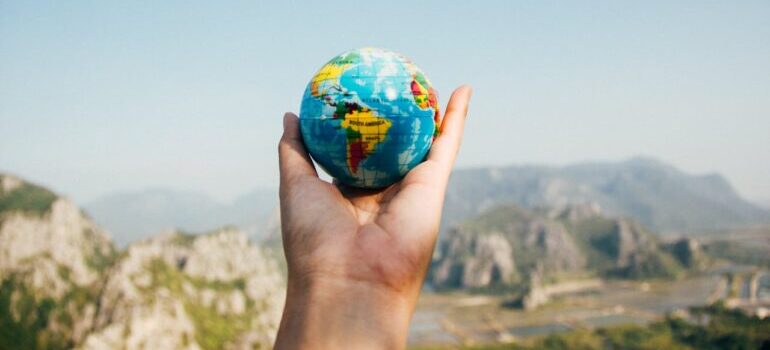 Person Holding World Globe Facing Mountain