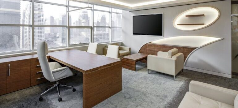 Gray Office Rolling Chair Near Brown Wooden Desk in Front of Flat Screen Tv on White Painted Wall