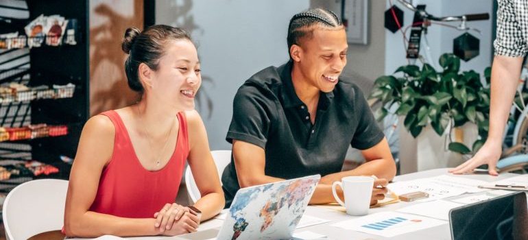 Smiling colleagues brainstorming at work around a table with laptops and documents.