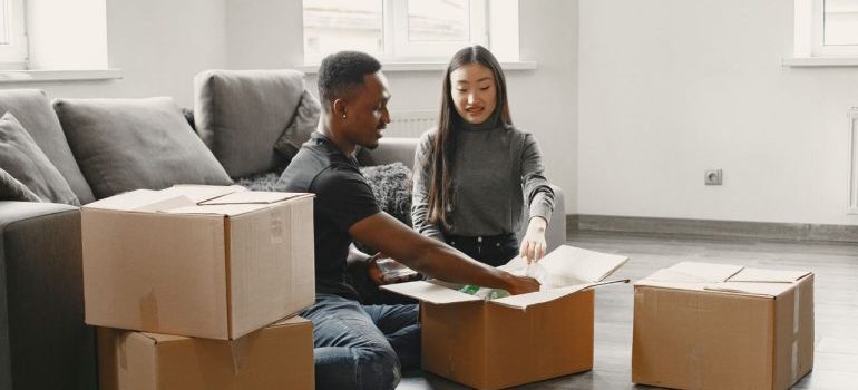 Happy couple unpacking moving boxes in their new apartment living room.